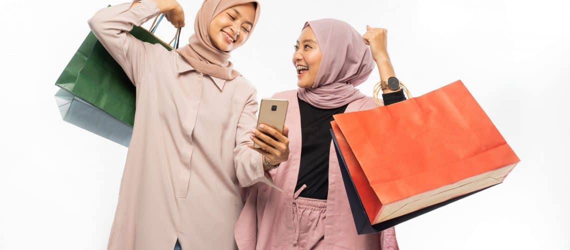 asian muslim young friend using smart phone and holding shopping bag together